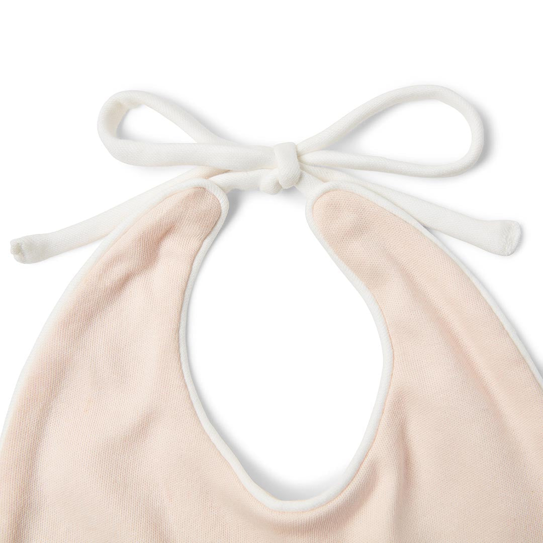 Bavoir souple rose clair pour bébé avec de longs cordons à nouer blancs, présenté à plat sur fond blanc.