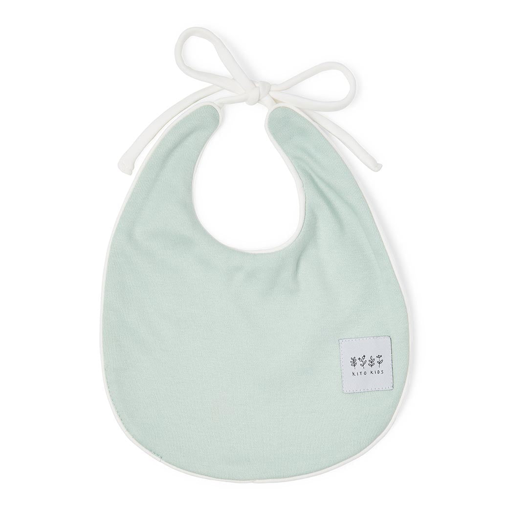Détail de l'encolure d'un bavoir vert d'eau montrant les finitions du liseré blanc et les cordons de serrage.