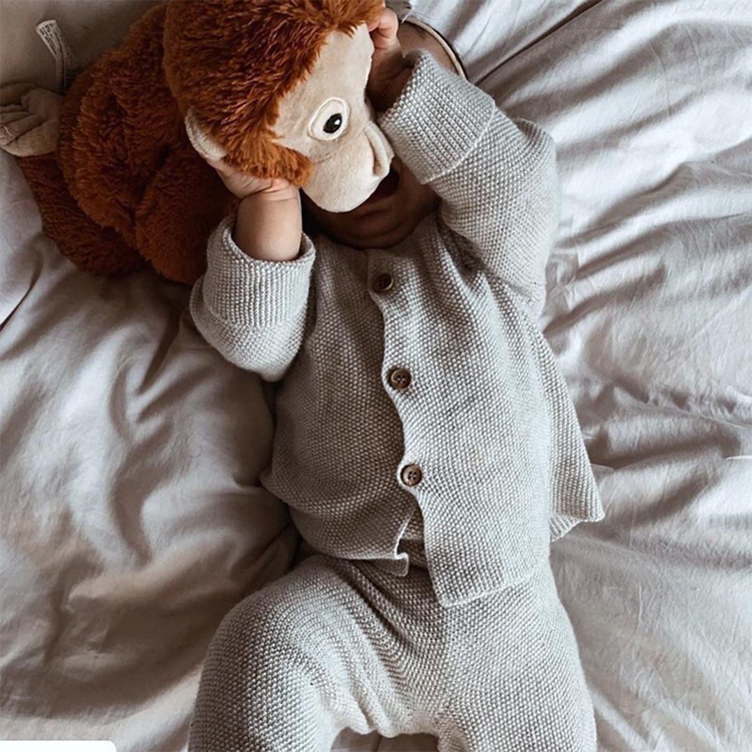 Nouveau-né portant un ensemble confortable en tricot de coton gris, allongé sur le dos et s'amusant avec une peluche de singe marron.