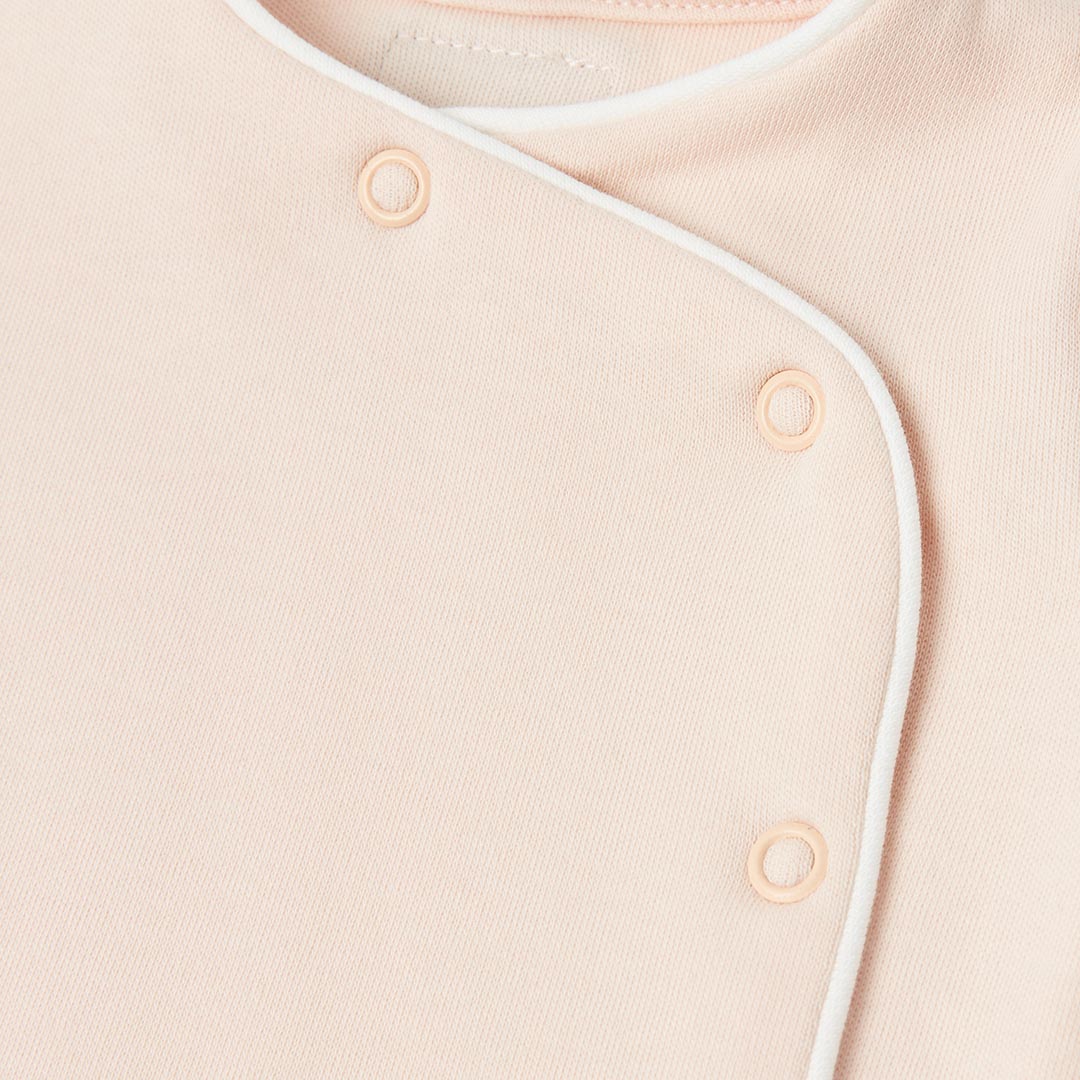 Détail des boutons-pression assortis et de l'encolure croisée d'un pyjama de naissance confortable pour bébé.