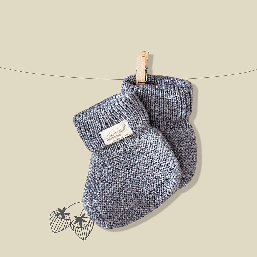 Petits chaussons de naissance pour bébé tricotés en maille grise, suspendus à un fil avec une pince à linge en bois.