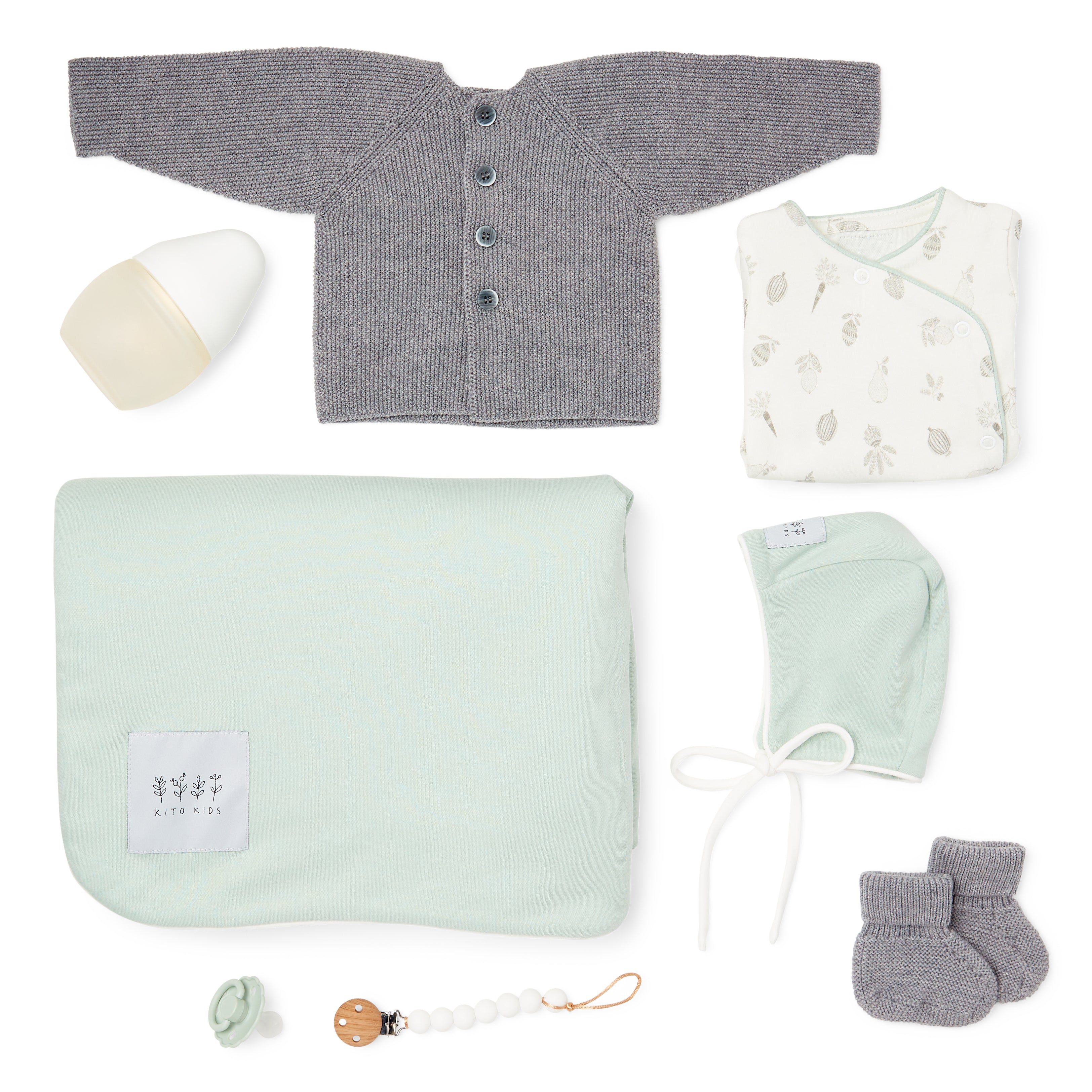 Coffret naissance Kito Kids avec couverture vert sauge, cardigan en laine mérinos gris, bonnet, chaussons, body imprimé, biberon et attache-tétine.