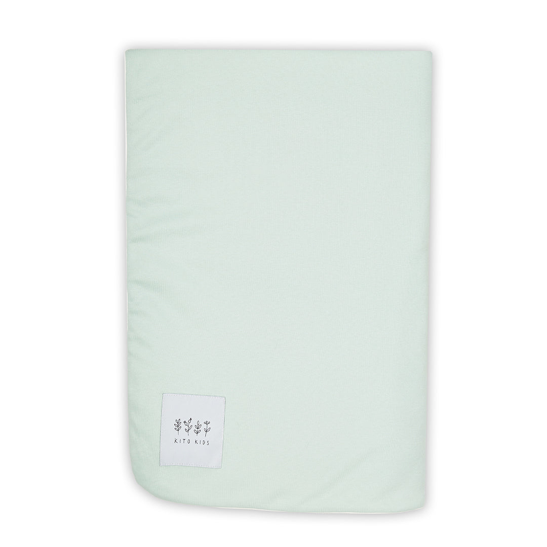 Couverture pour bébé pliée montrant sa double face vert d'eau et blanche imprimée, avec l'étiquette logo de Kito Kids.