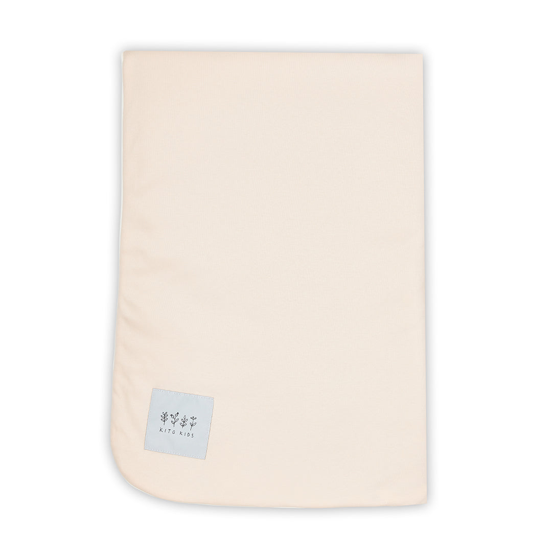 Couverture pour bébé pliée dévoilant sa double face rose pêche et blanche à motifs citrons, avec l'étiquette logo Kito Kids.
