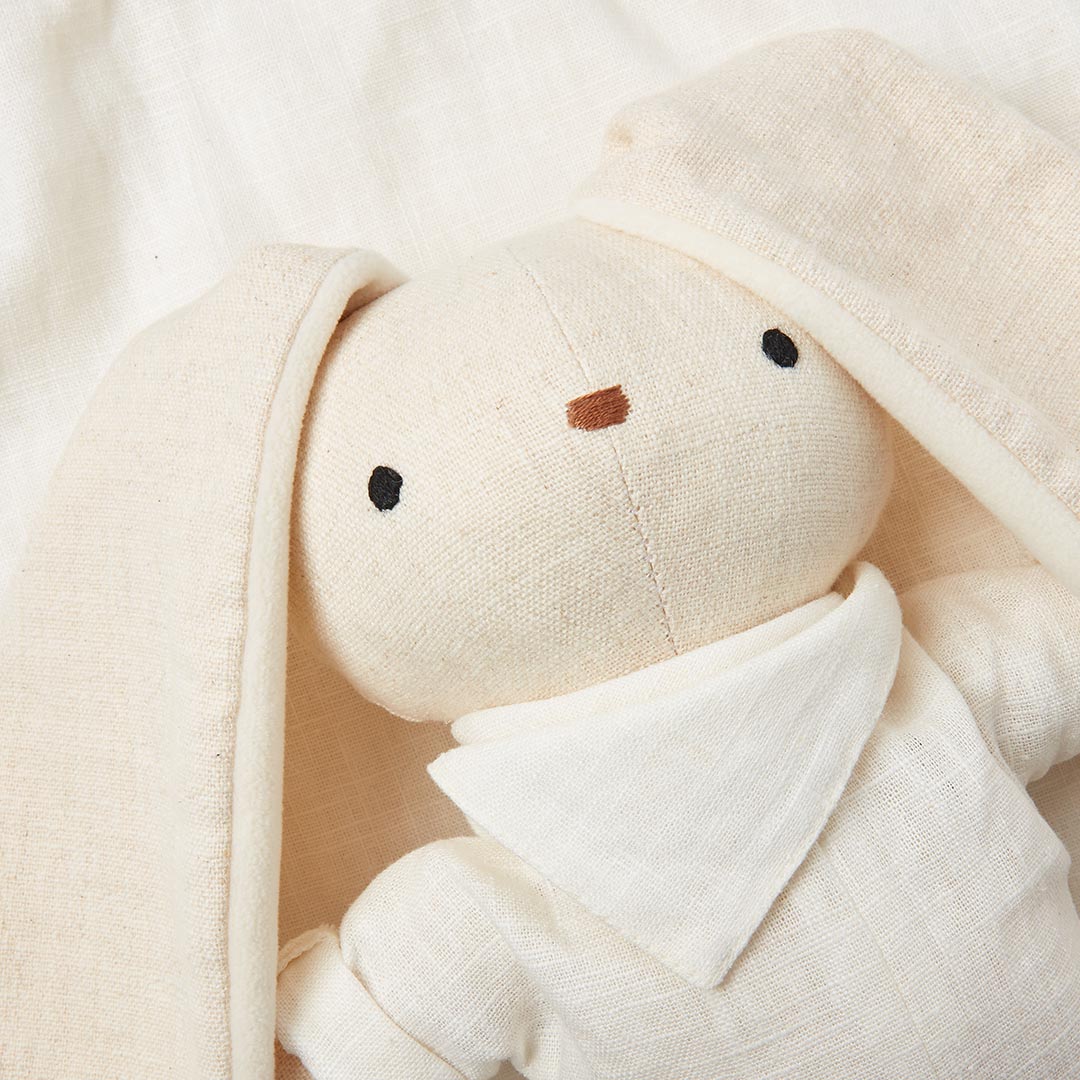 Gros plan sur la tête d'une peluche lapin écru en lin et coton doux montrant ses yeux et son nez brodés.