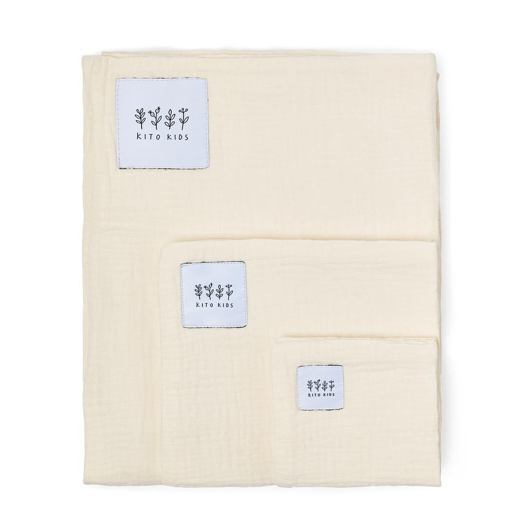 Détail du pliage d'un lange en mousseline de coton de couleur blanc cassé, mettant en valeur son tissage léger.