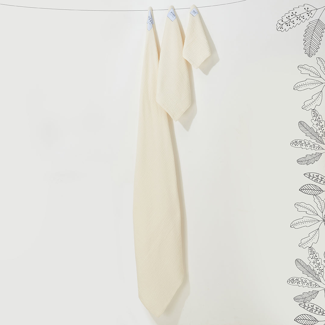 Lot de trois langes en mousseline de coton jaune pastel de tailles différentes suspendus sur un fil.