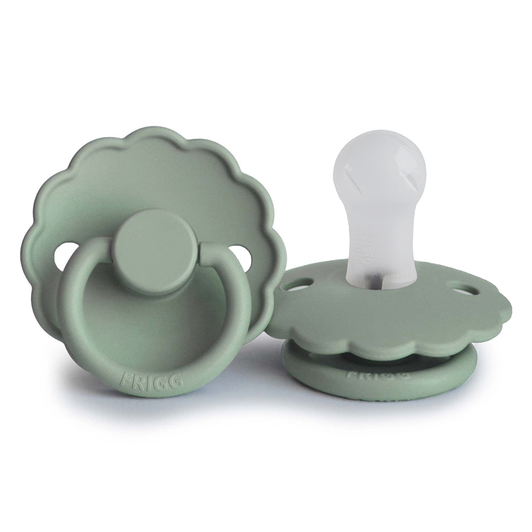 Tétine modèle Daisy de couleur vert sauge, l'une de face montrant la collerette en forme de fleur et l'autre de profil révélant l'embout en silicone blanc.