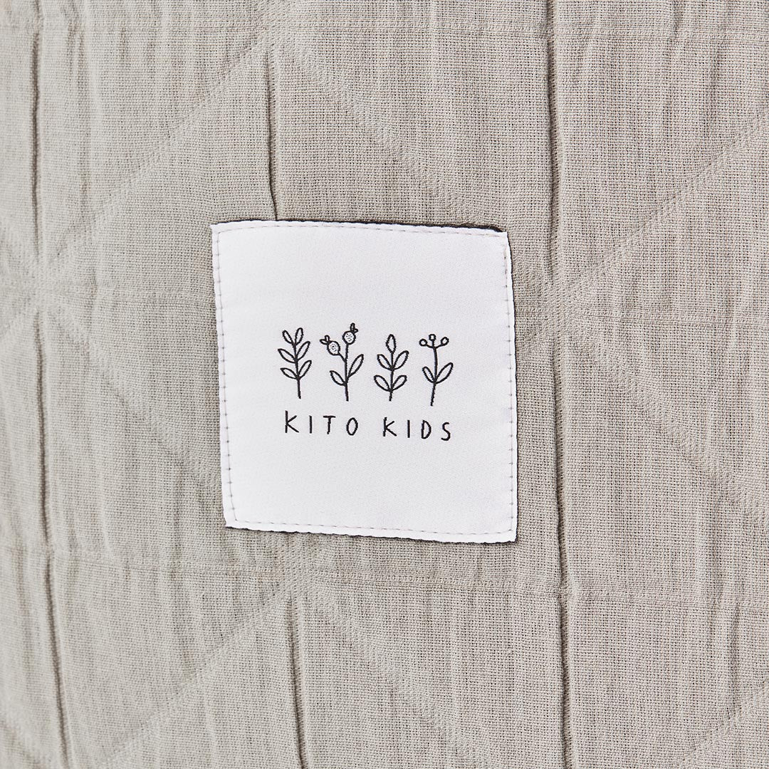 Détail de la texture matelassée géométrique beige et de l'étiquette logo Kito Kids cousue sur un sac pour bébé.