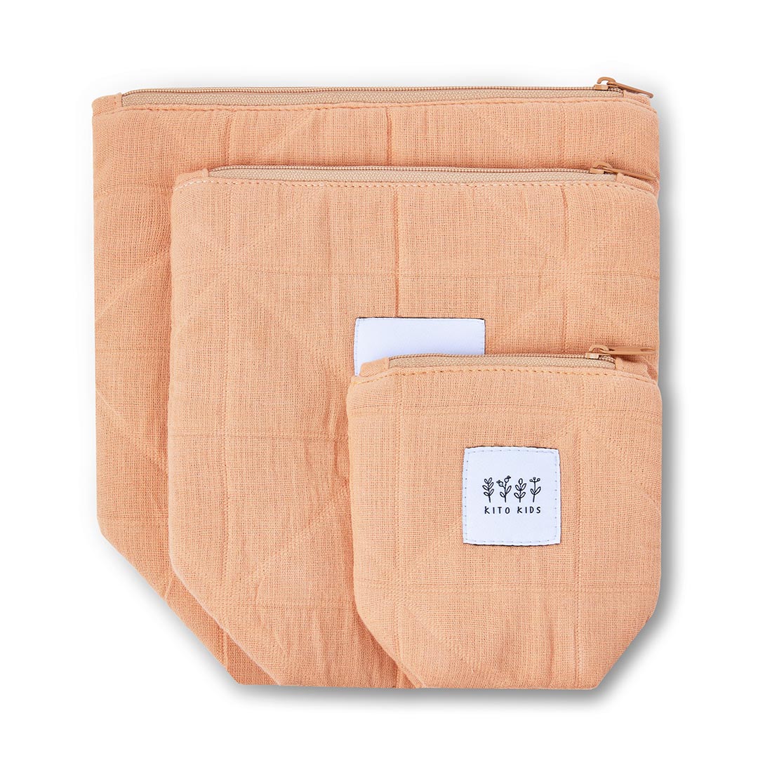 Trousses de toilette pour bébé terracotta et crème en coton bio, accompagnées de produits de soins bio.
