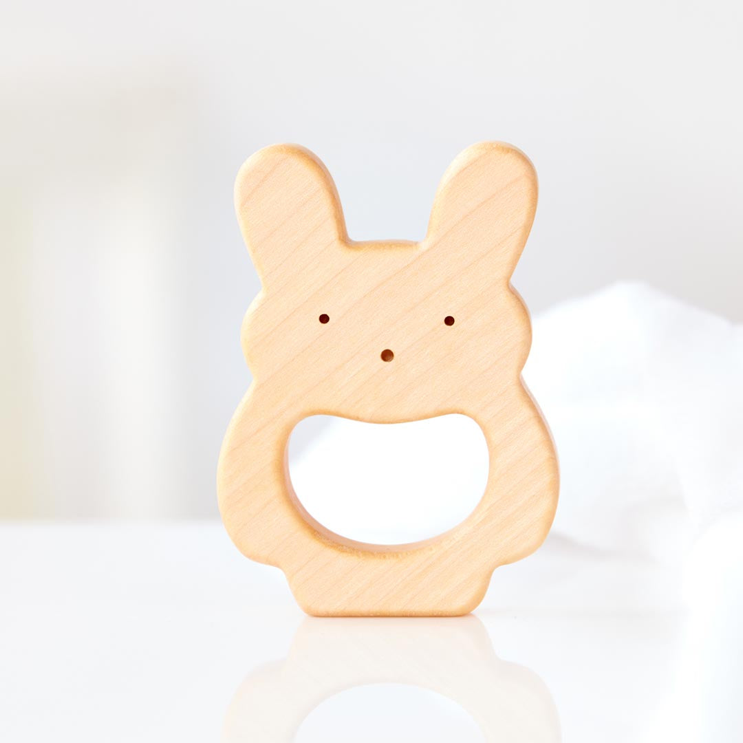 Hochet et anneau de dentition en forme de lapin en bois naturel non traité, spécialement conçu pour soulager efficacement et naturellement les poussées dentaires de bébé.
