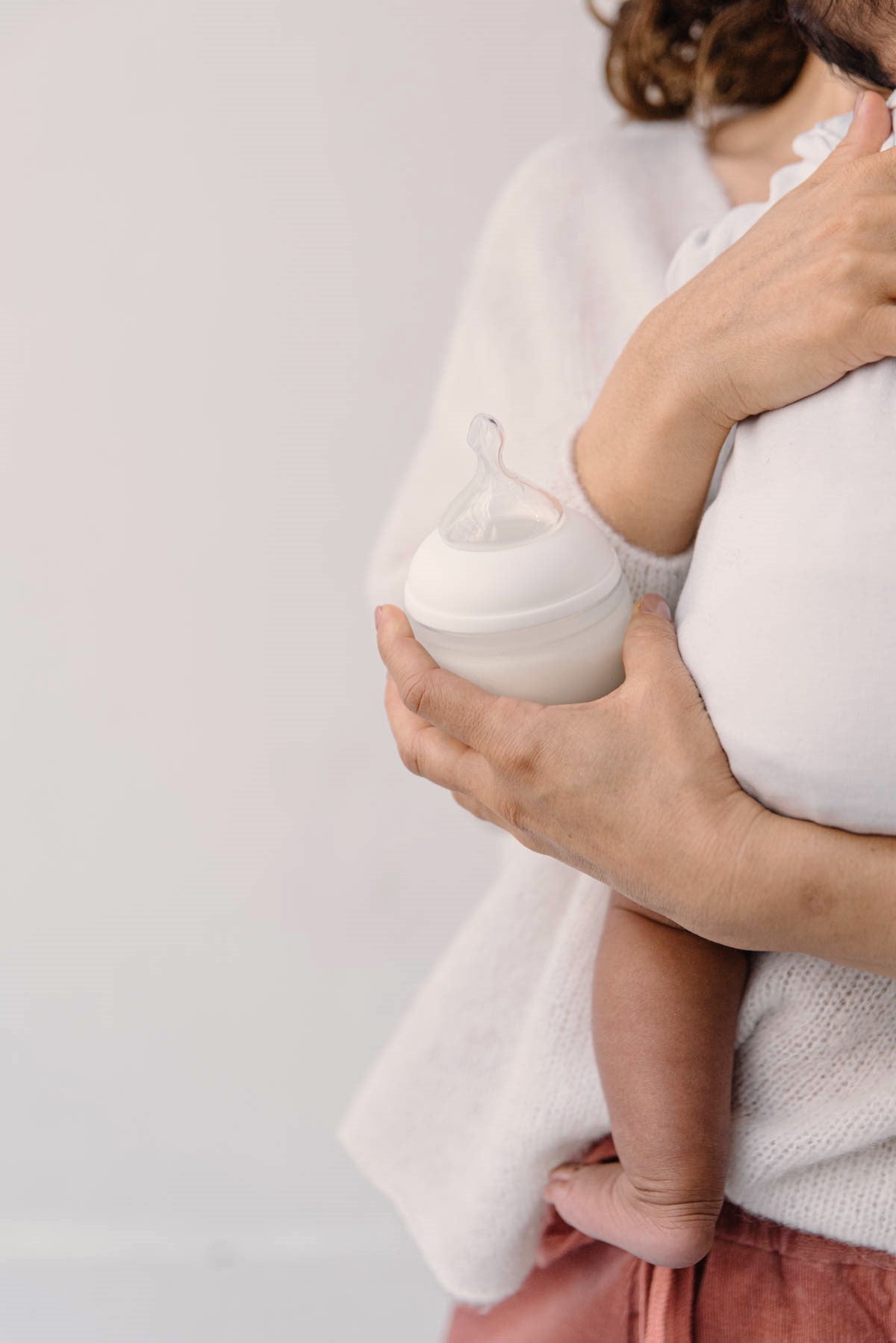 Maman tenant son nourrisson tout en tenant un biberon Élhée en silicone souple blanc, idéal pour un allaitement mixte serein et sans confusion sein-tétine.