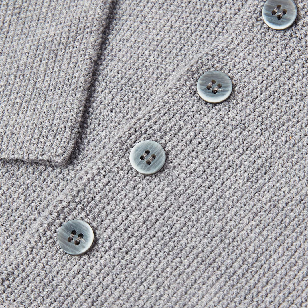 Détail rapproché des boutons ronds et de la texture en maille tricotée d'un gilet de naissance gris pour bébé.