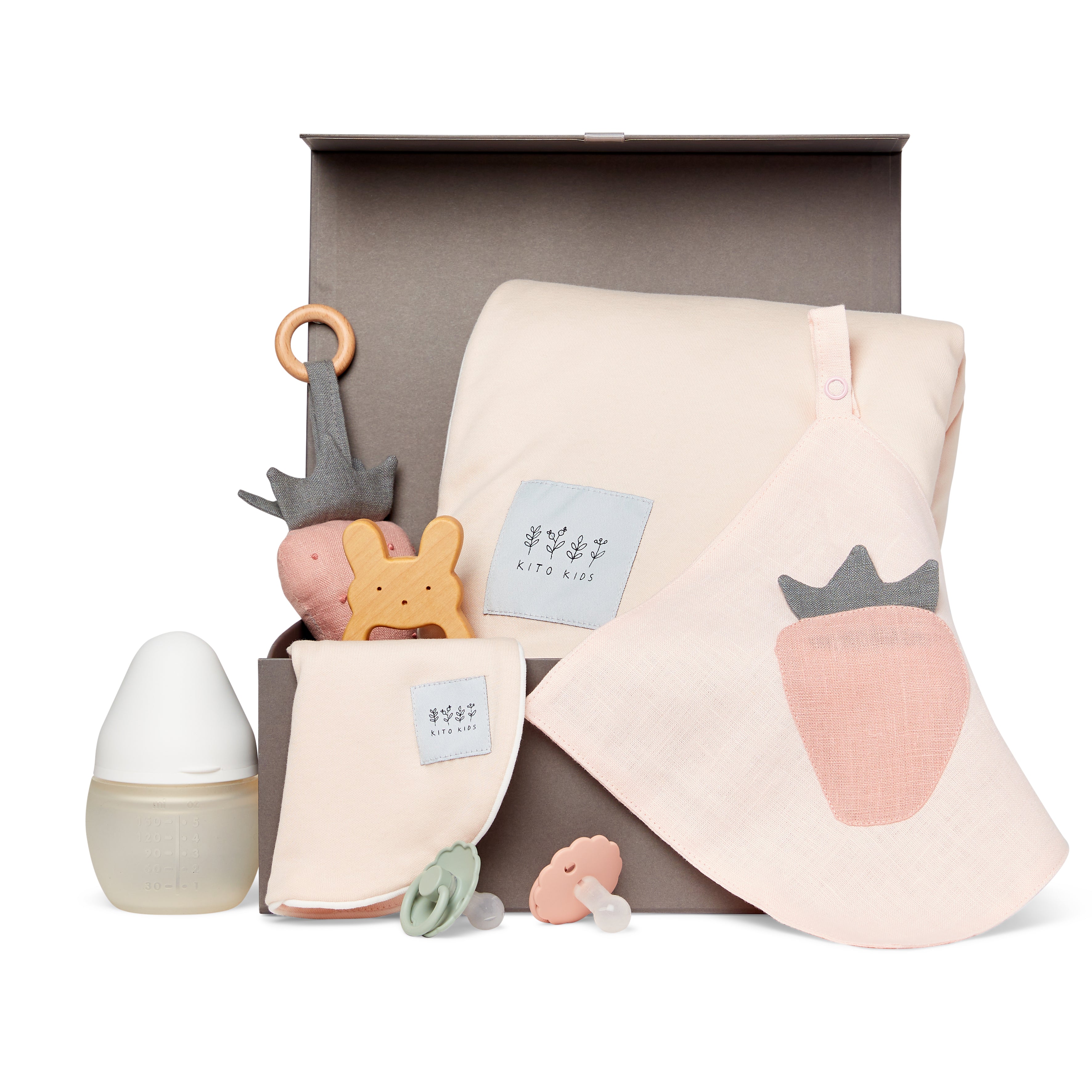 Coffret cadeau de naissance écoresponsable Kito Kids comprenant un grand lange rose poudré, un bavoir assorti avec motif fraise, un hochet en bois, un biberon et des tétines pour bébé.