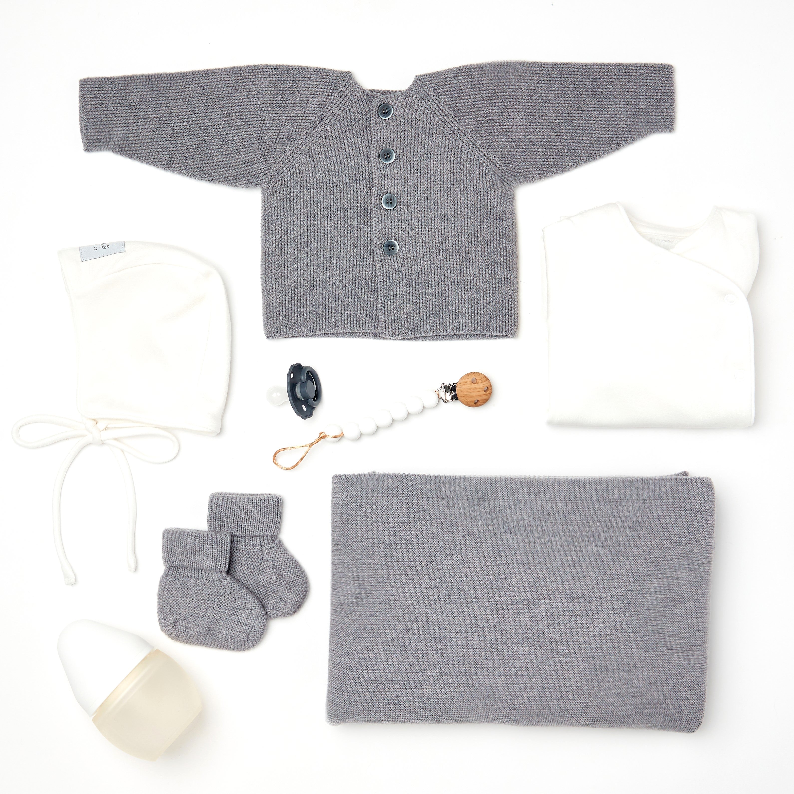 Coffret naissance Kito Kids avec couverture grise, cardigan en laine mérinos gris, bonnet blanc, body blanc, chaussons, biberon et attache-tétine.