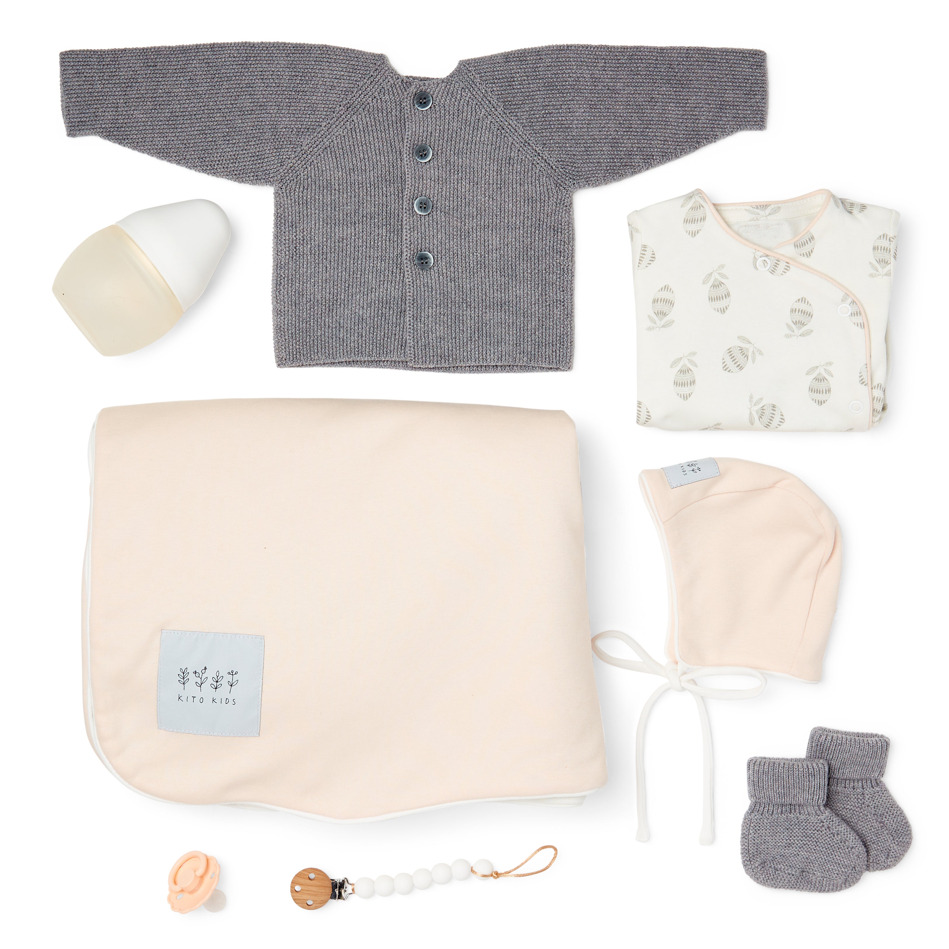 Coffret naissance Kito Kids avec couverture rose poudré, cardigan en laine mérinos gris, bonnet, body imprimé, chaussons, biberon et attache-tétine.