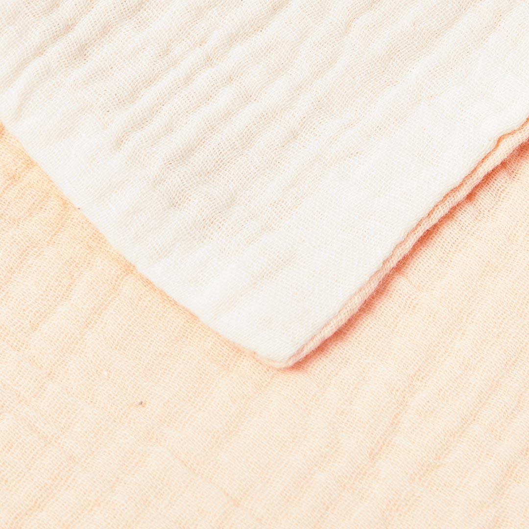 Gros plan sur la superposition et la texture douce d'un lange blanc et d'un lange pêche en mousseline de coton.