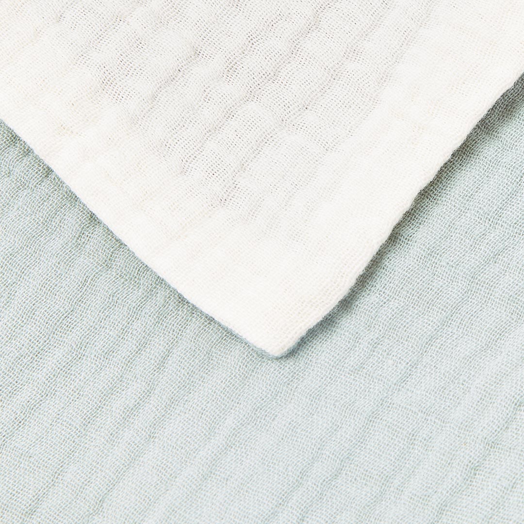 Gros plan sur la superposition et la texture d'un lange blanc et d'un lange vert sauge en mousseline de coton.