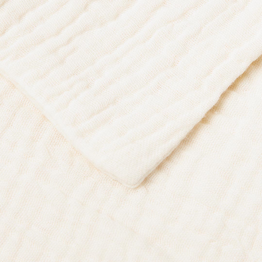 Gros plan sur la texture gaufrée et ultra-douce d'un lange pour bébé en double gaze de coton de couleur crème.