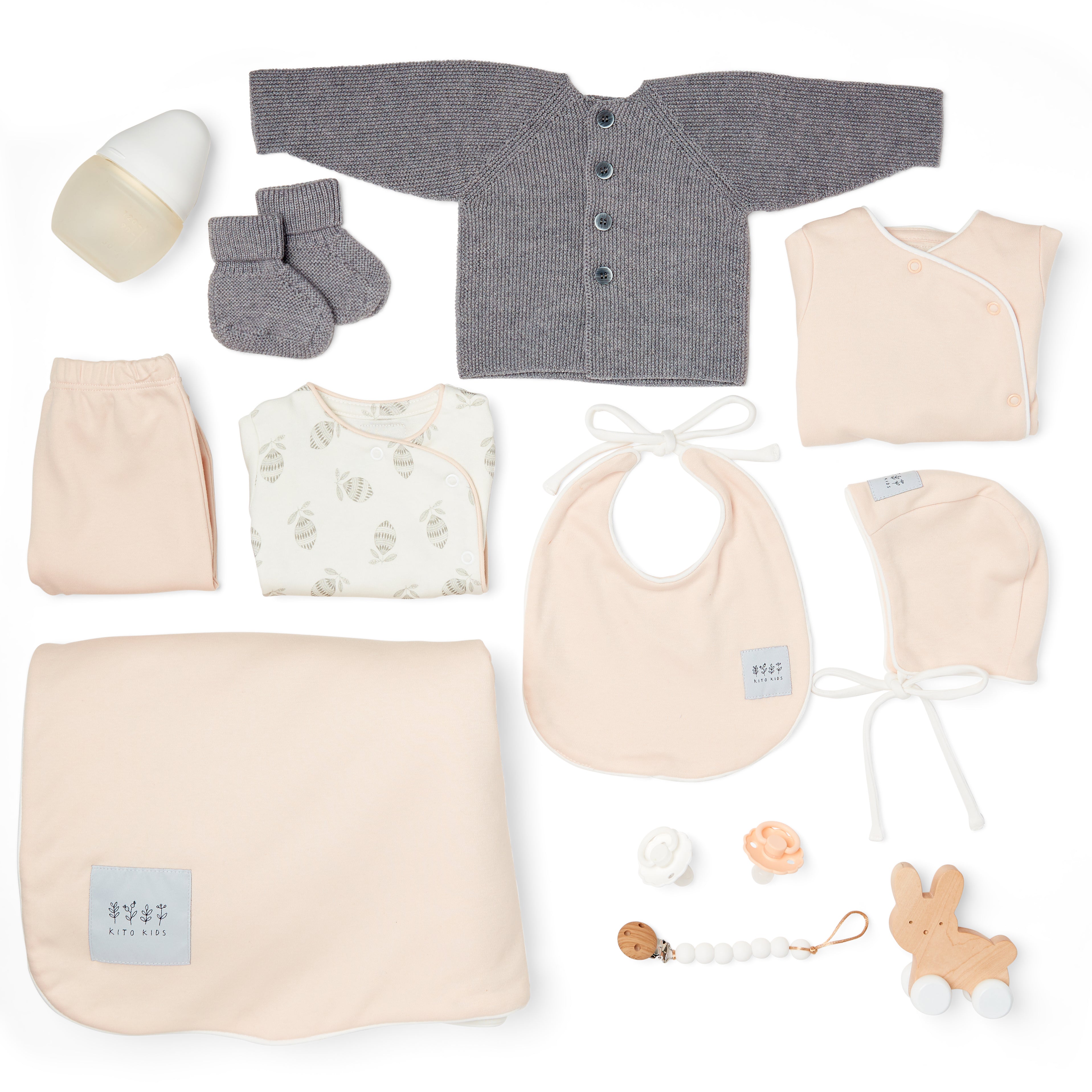 Essentiels de naissance pour bébé en rose poudré et laine mérinos comprenant couverture, cardigan, bonnet, bavoir, chaussons, vêtements, attache-tétine et accessoires Kito Kids.