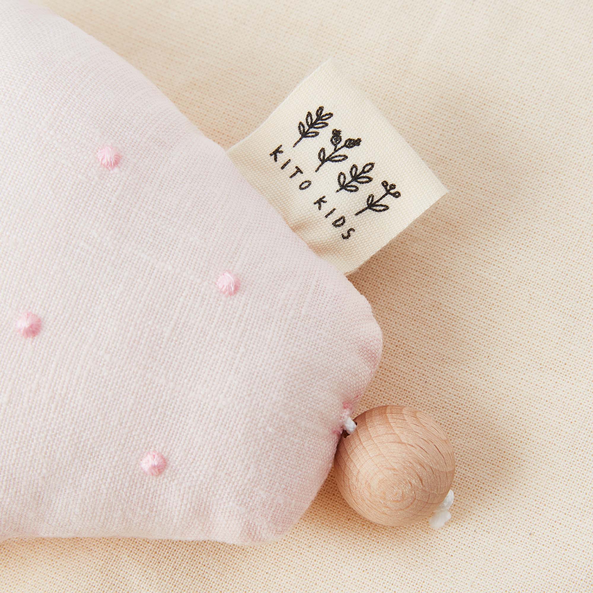 détails d'un hochet fraise rose en tissu avec sa perle en bois et l'étiquette de la marque Kito Kids.