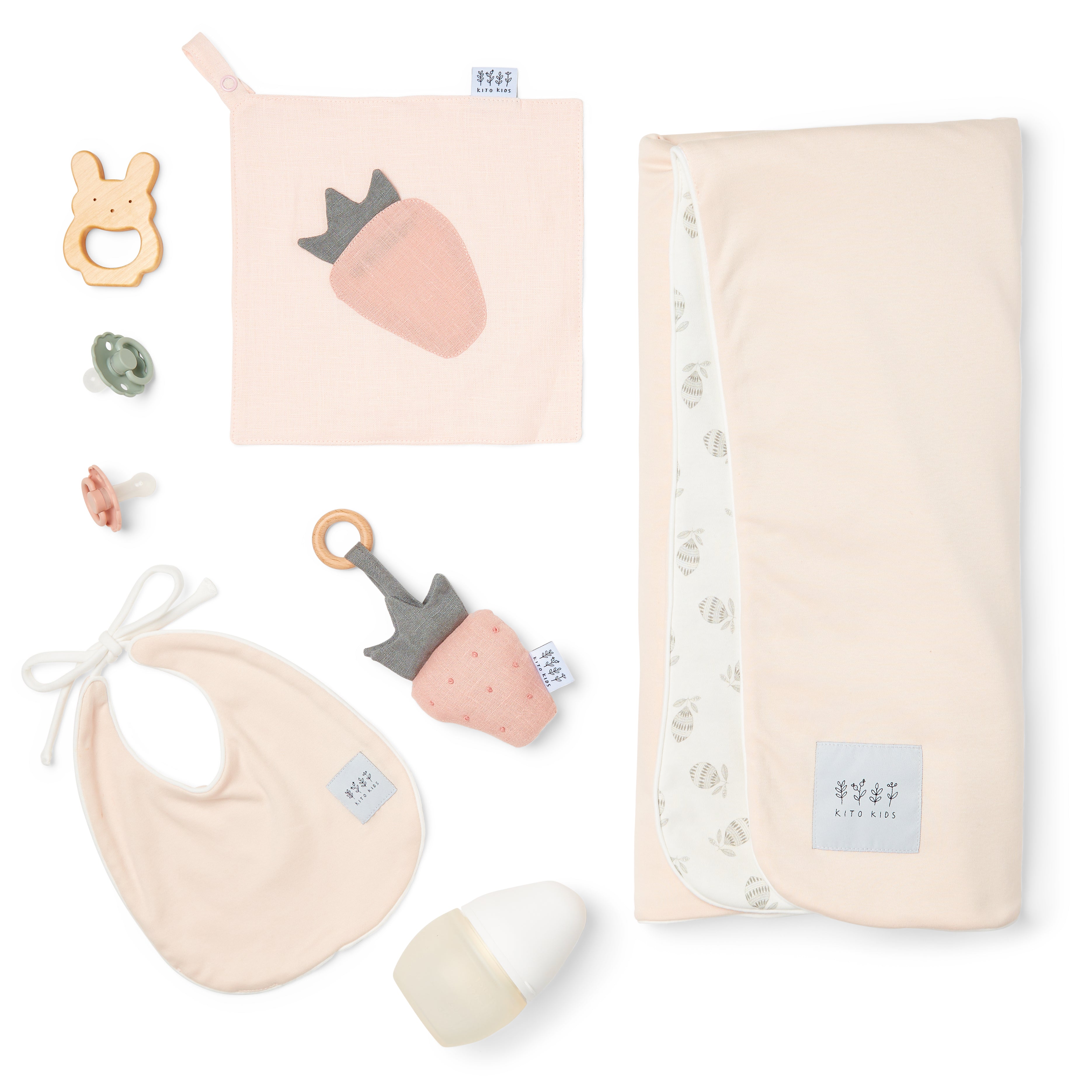 Kit de naissance complet pour bébé Kito Kids comprenant un grand lange rose poudré, un bavoir, un doudou plat fraise, un hochet en bois, un biberon et des tétines.