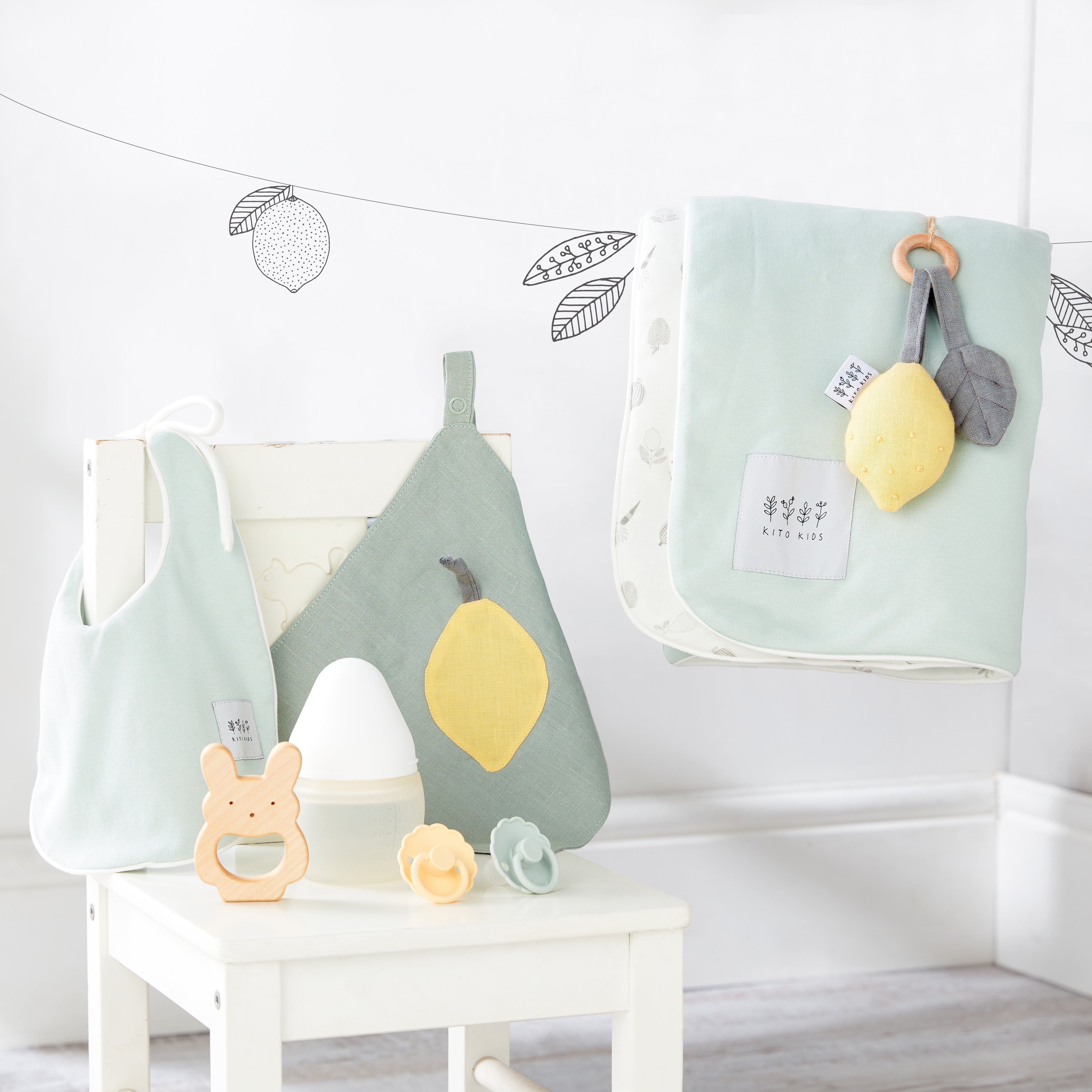 Kit de naissance écoresponsable vert menthe et jaune comprenant un bavoir, un lange en coton bio, un hochet en bois en forme de citron et un anneau de dentition Kito Kids.