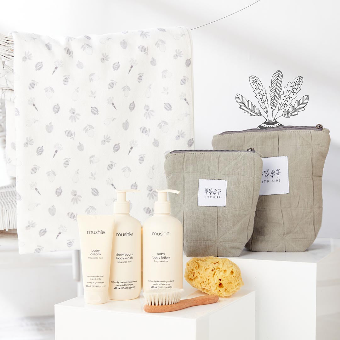 Serviette de bain blanche imprimée pour bébé à côté de deux trousses de toilette matelassées kaki Kito Kids et de crèmes de soin.