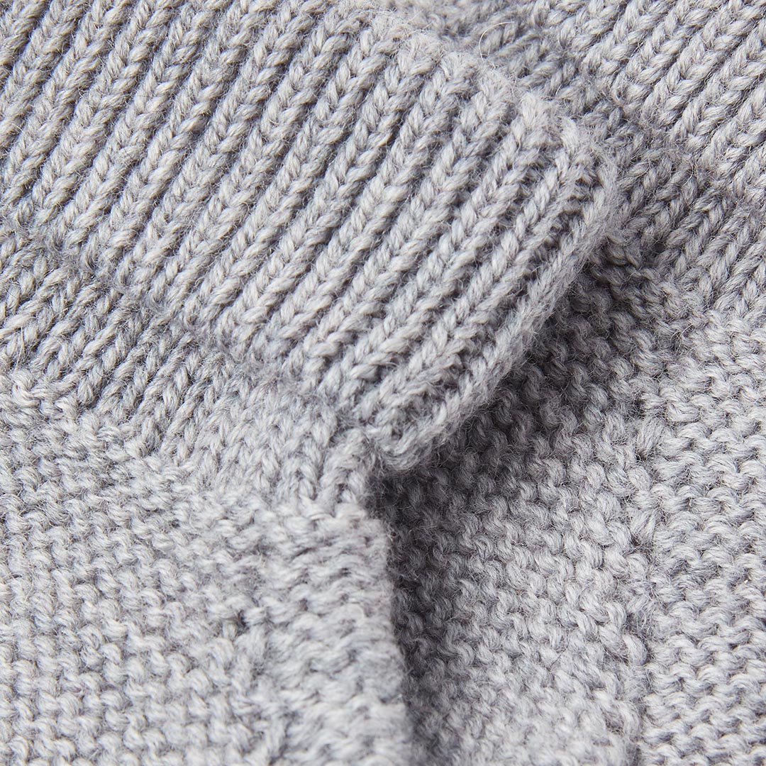 Gros plan détaillé sur la texture douce et régulière d'un tricot en laine grise pour vêtements et accessoires bébé.