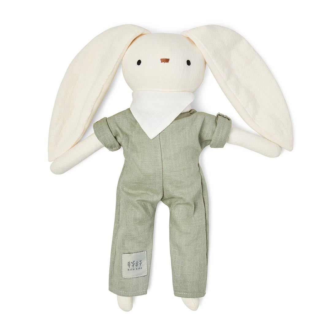 Peluche lapin pour bébé habillée en vert et présentée sur son sac de transport à coulisse en lin vert.