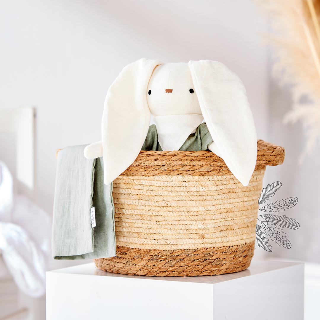 Doudou lapin blanc de la marque Kito Kids avec de grandes oreilles tombantes, habillé d'un vêtement en lin vert sauge.