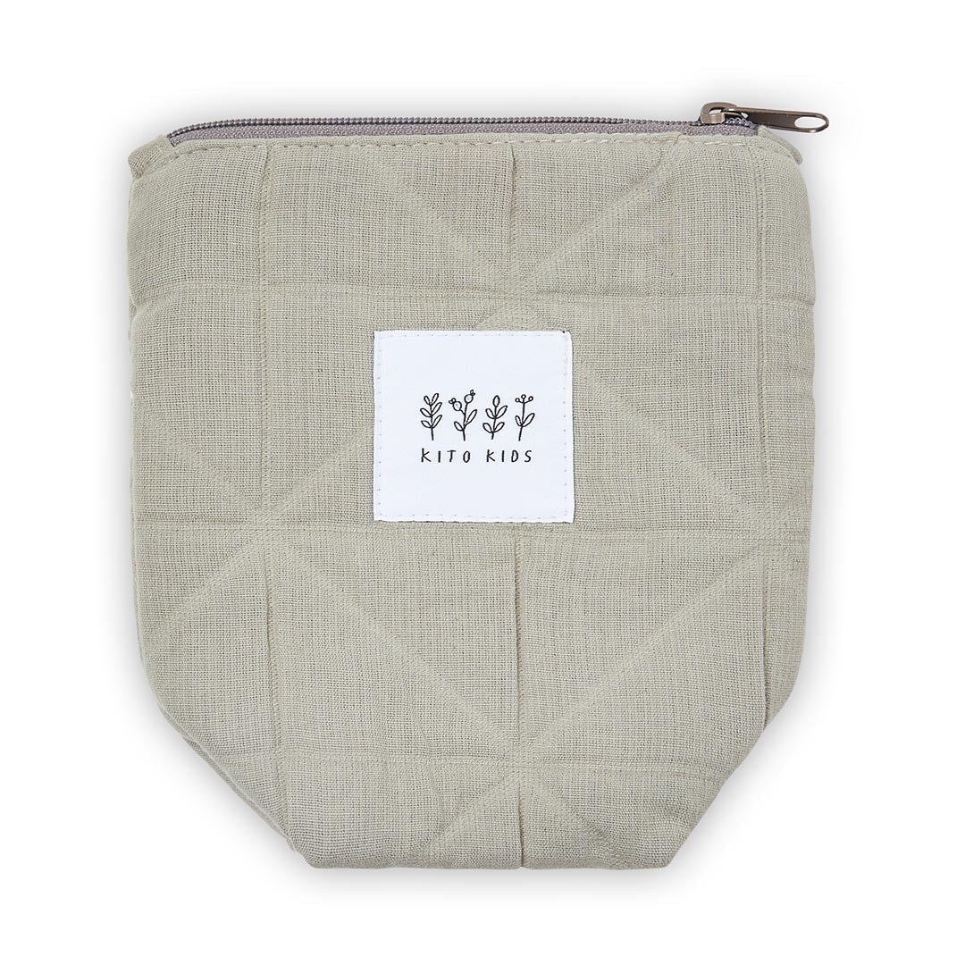 pochettes de toilette en tissu kaki de Kito Kids entourées de crèmes, shampoing pour bébé, brosse en bois et serviette de bain à motifs.
