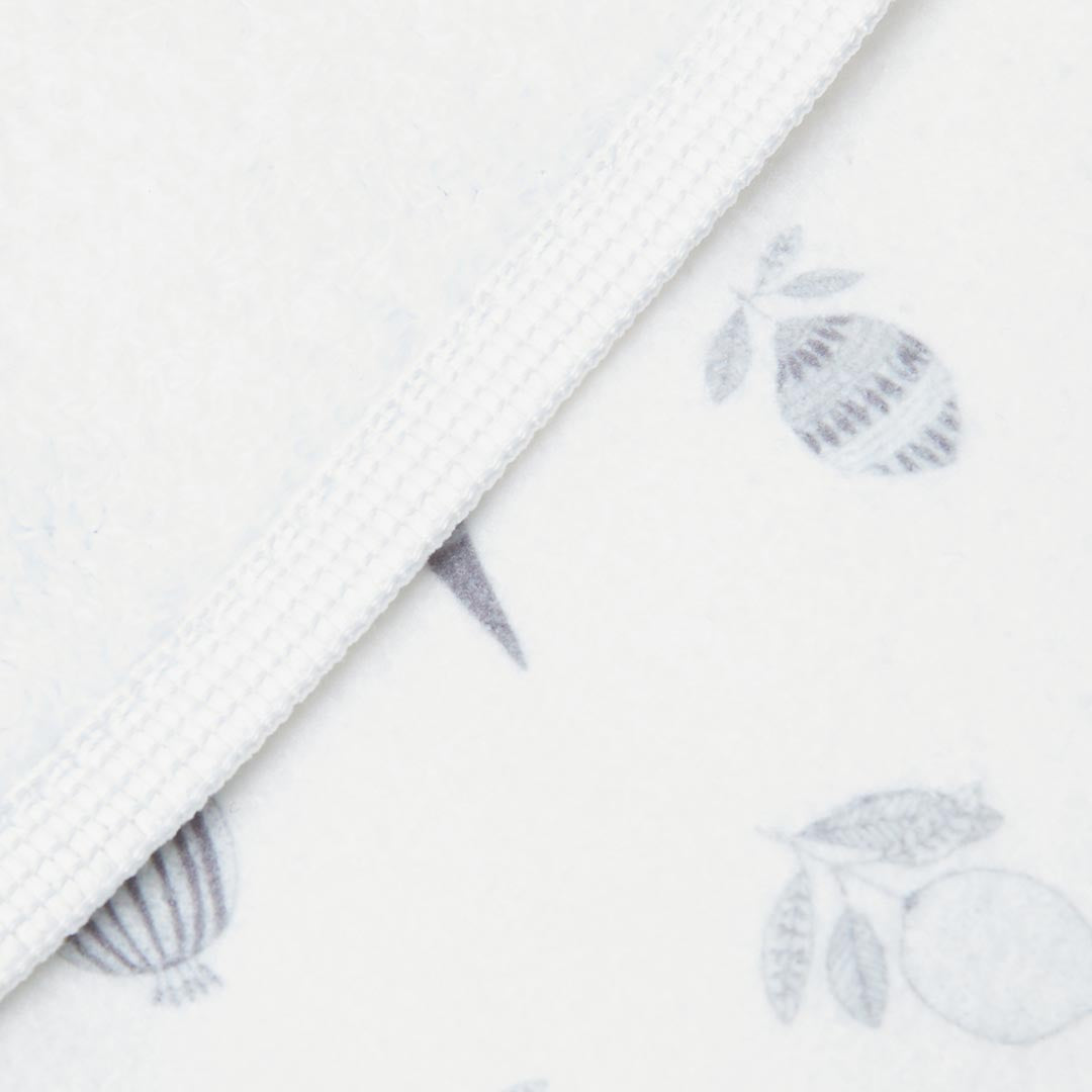 Serviette de bain pour bébé blanche en coton doux, pliée pour laisser apparaître une doublure en éponge absorbante et des motifs d'agrumes gris.