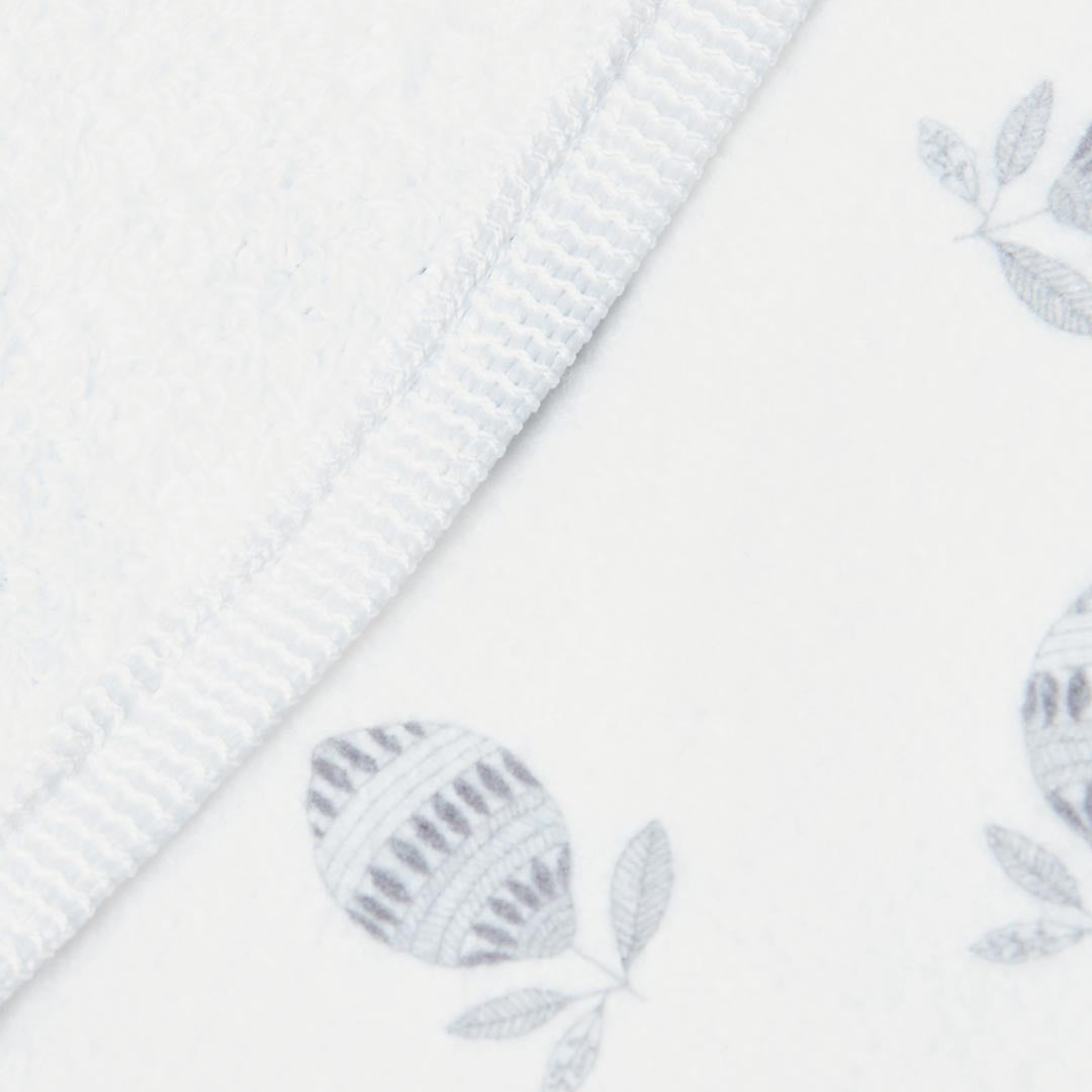 Détail d'un drap de bain Kito Kids blanc en coton épais, mettant en valeur des illustrations délicates d'agrumes