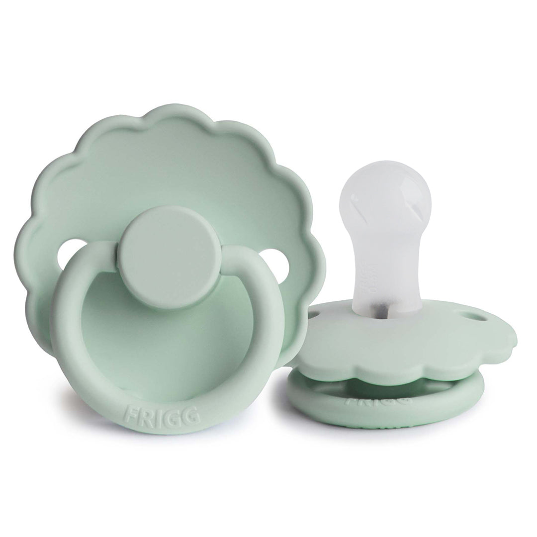 Sucette pour bébé Frigg en forme de marguerite vert menthe pastel avec une collerette festonnée et une tétine en silicone souple.